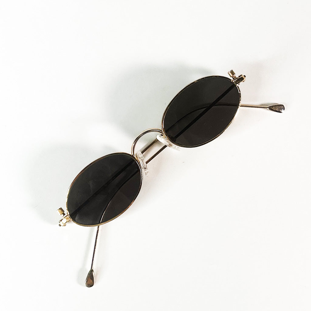  vue de dessus d’une paire de lunettes Paco Rabanne en métal doré, verres ovales noirs, branches croisées sur fond blanc